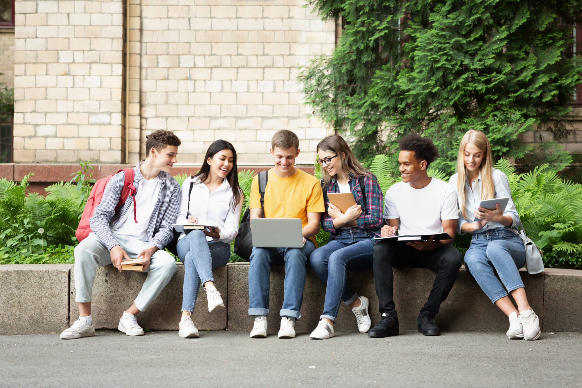 Students outside on cement wall smiling at computer
